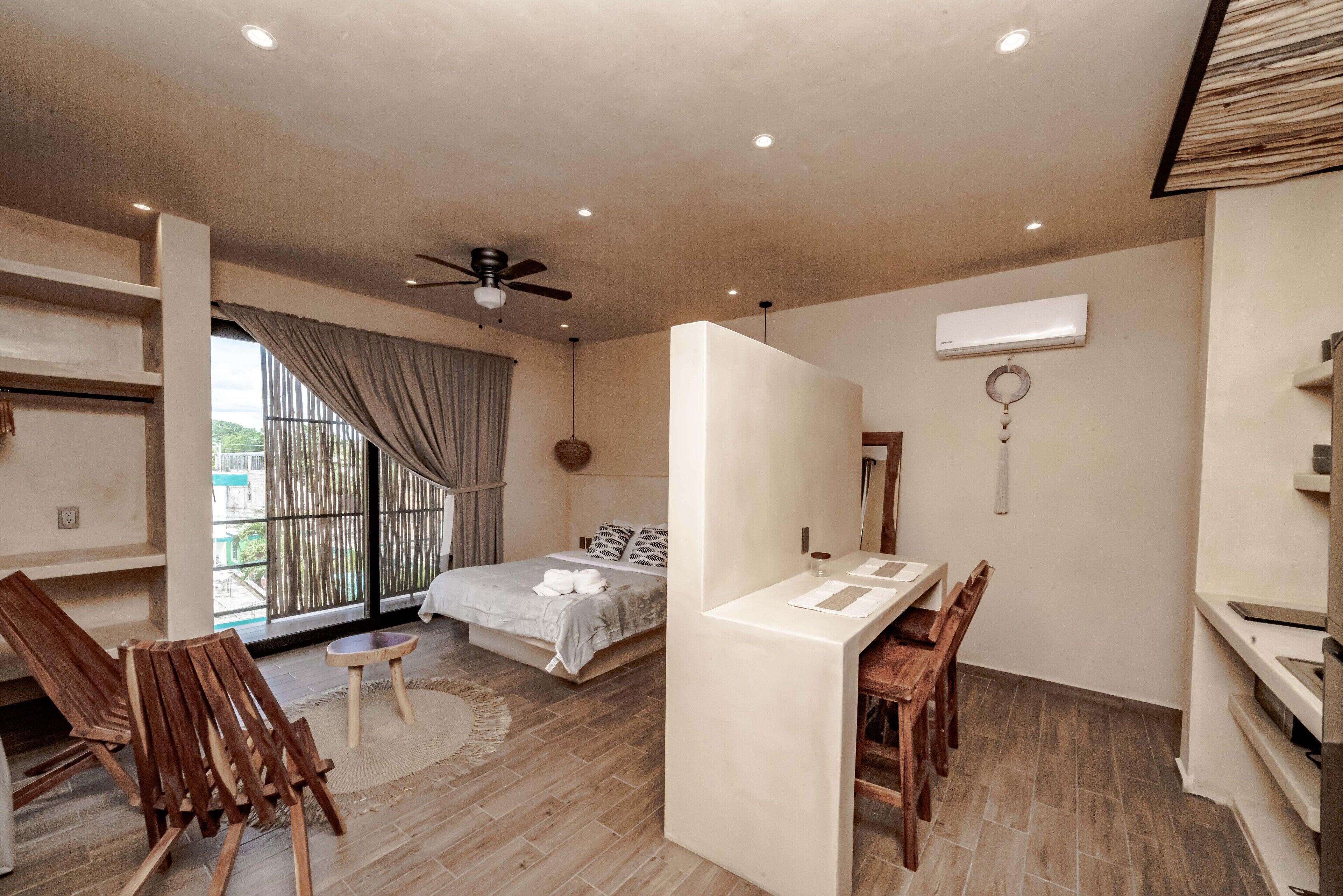 A bedroom with a bed, a desk, a chair, a ceiling fan, and a window with curtains.