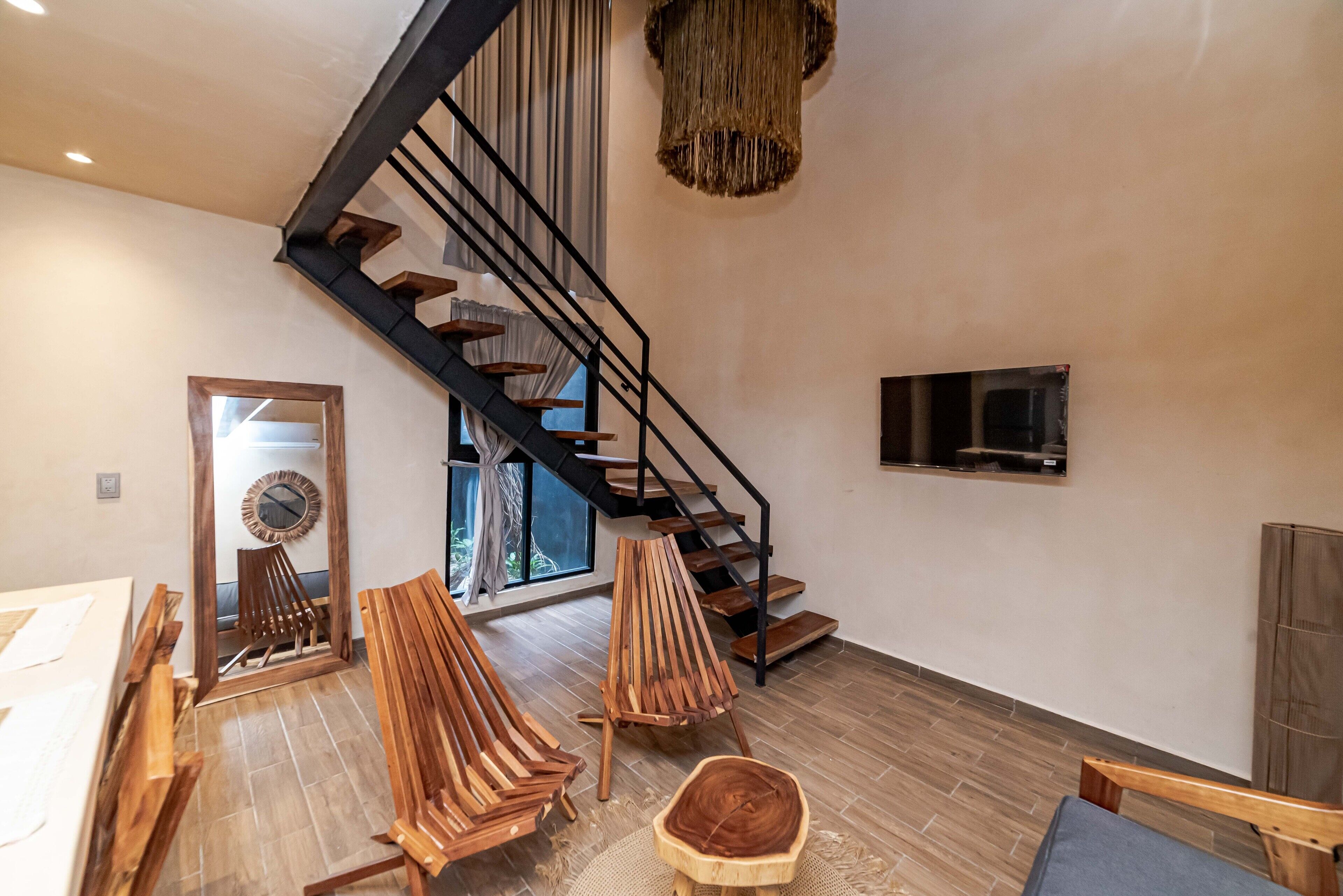 A spacious living area with a wooden floor, a staircase with a black railing, and a large window.