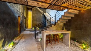 A modern interior with a concrete staircase, a wooden table with stools, and a ceiling made of wooden slats. - The Teodoro (Tulum)