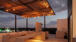 A rooftop terrace with a wooden pergola, string lights, and a view of a cityscape at dusk. - The Teodoro (Tulum)