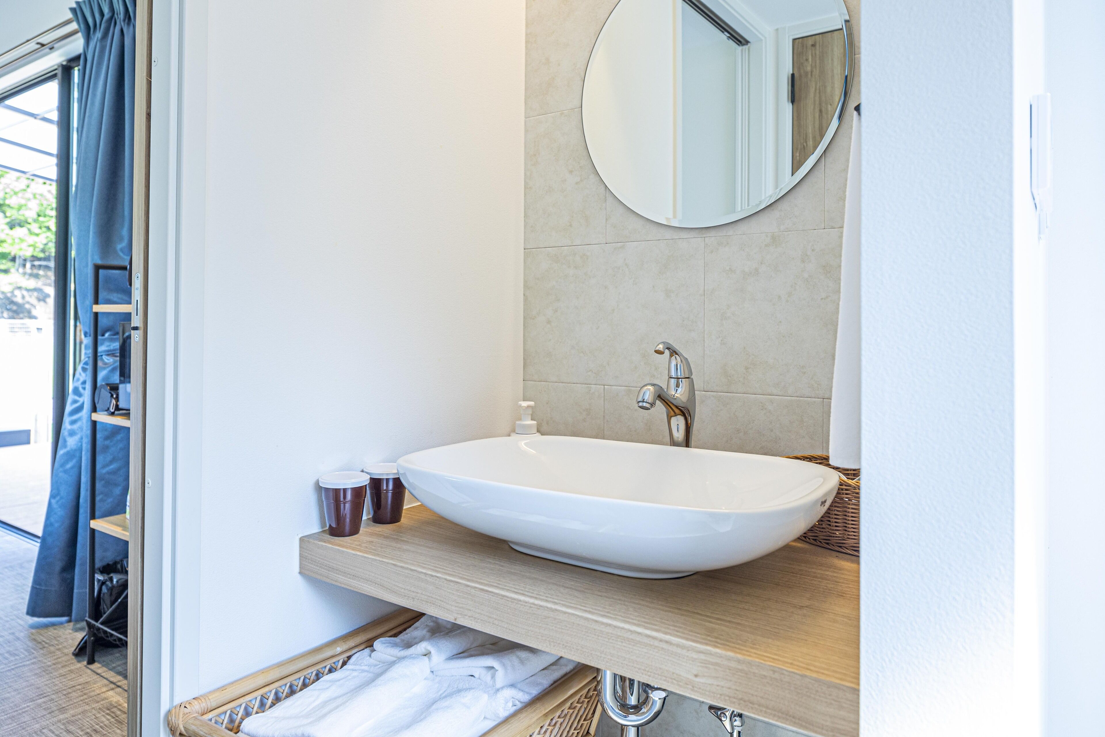 A bathroom with a white sink, a mirror, and a wooden shelf.