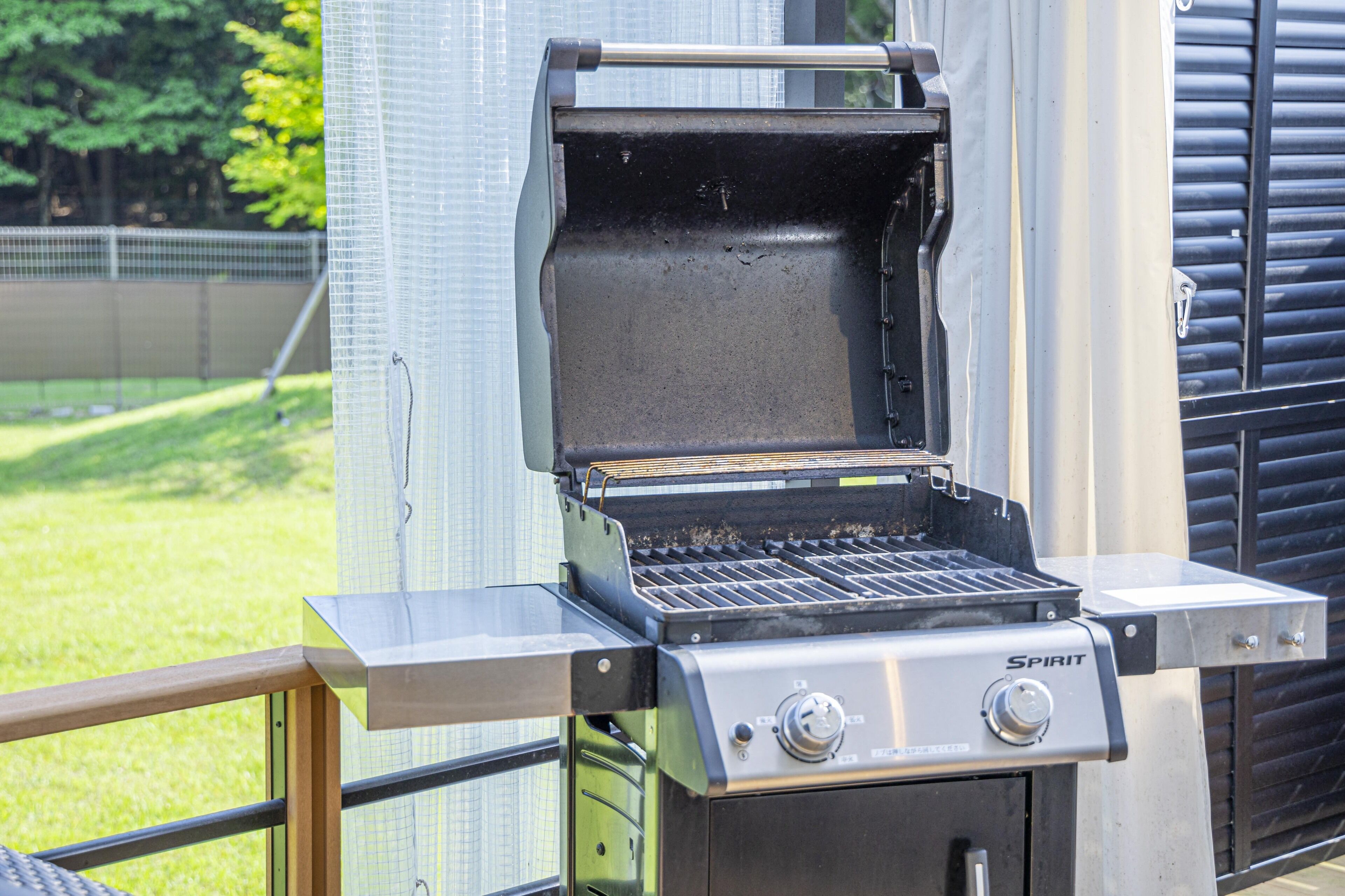 En Spirit transportabel grill med digitalt kontrolpanel, placeret udendørs med udsigt til en græsplæne og et hegn i baggrunden.