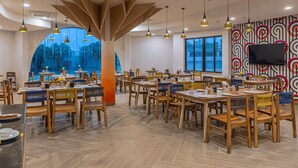 A spacious dining area with multiple tables and chairs, large windows with a view, and hanging pendant lights.