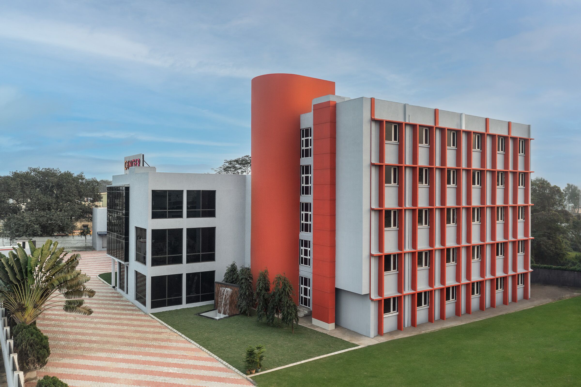A modern building with a red and white facade, large windows, and a central courtyard with a striped pathway.