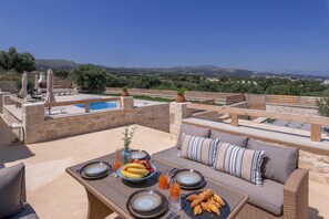 Terraço no telhado com piscina, mesa de jantar com pratos e sofá com almofadas.