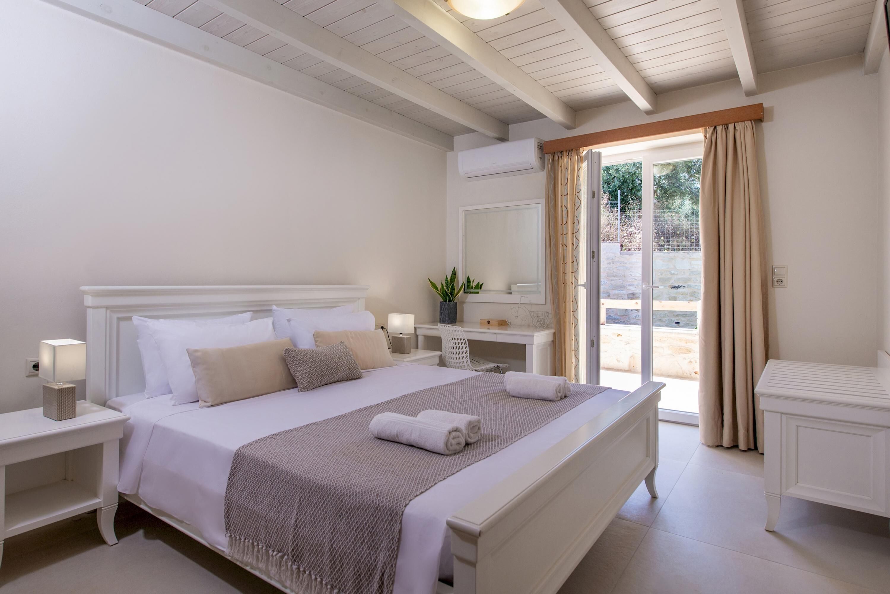 A neatly arranged bedroom with a bed, bedside tables, a desk, and a large window with curtains.