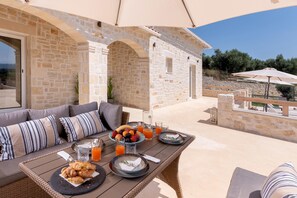 Un área de comedor al aire libre con paredes de piedra, una mesa de mimbre y vista al mar.