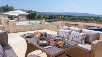 An outdoor dining area with a pool, wicker furniture, and a scenic view.