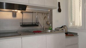 Une cuisine moderne avec des armoires blanches, une hotte de cuisinière en acier inoxydable, un porte-ustensiles suspendu et une fenêtre ornée de rideaux légers.