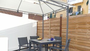Une terrasse extérieure avec une table et des chaises, une clôture en bois et un parasol blanc.
