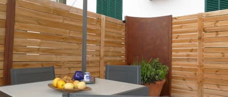 A small outdoor dining area with a table and chairs, a potted plant, and a wooden fence.