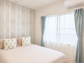 Un dormitorio con una cama, una ventana con cortinas y un aire acondicionado instalado en la pared.