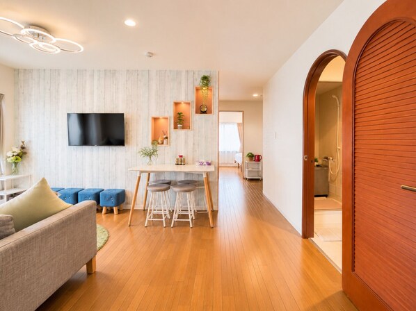 Una sala de estar moderna con un sofá, un comedor con taburetes, un televisor en la pared y piso de madera.