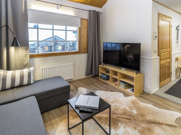 Un salon moderne avec un canapé, un téléviseur posé sur un meuble en bois, une cheminée et une vue sur un bâtiment à l’extérieur.