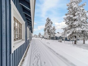 Una calle nevada con un edificio azul a la izquierda y árboles cubiertos de nieve a la derecha.