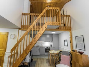 Una escalera de madera de varios niveles que conecta dos pisos, una cocina con electrodomésticos modernos y un comedor con mesa y sillas.