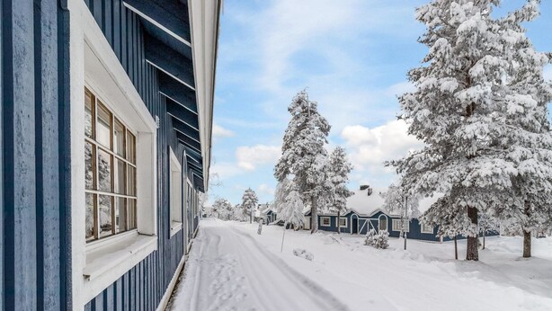 Un sentier enneigé mène à une maison à l’extérieur bleu et dotée de grandes fenêtres.