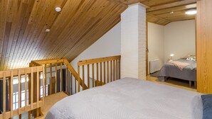 Une chambre avec un grand lit, un escalier en bois et une cheminée en briques blanches.