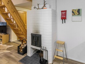 A room with a white brick fireplace, a wooden staircase, a small wooden stool, and a calendar on the wall.