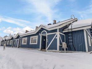 Una hilera de edificios azules con detalles blancos, cubiertos de nieve, y una persona caminando sobre la nieve.