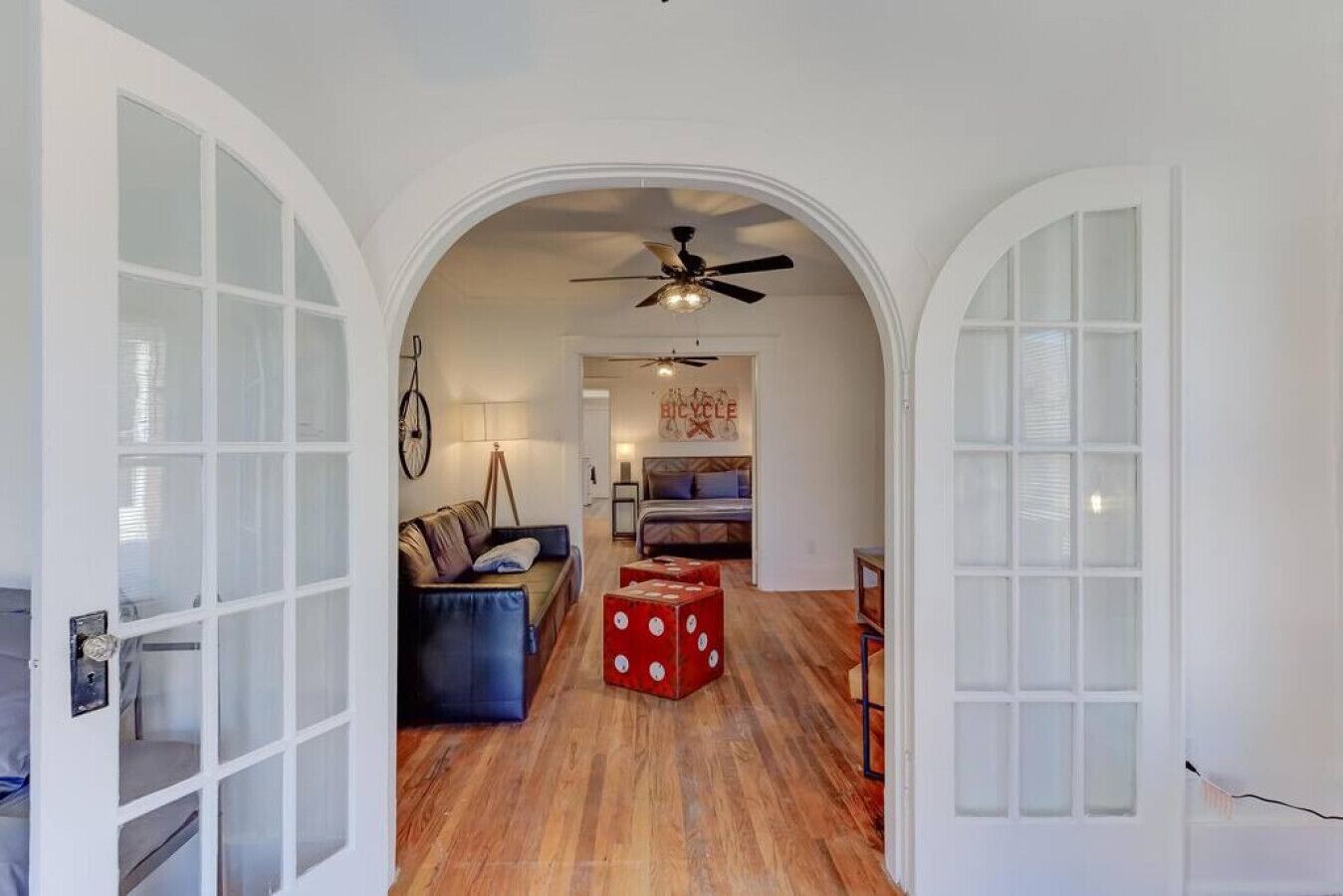 Un intérieur avec un plancher en bois, un canapé, un cube rouge et un ventilateur de plafond.