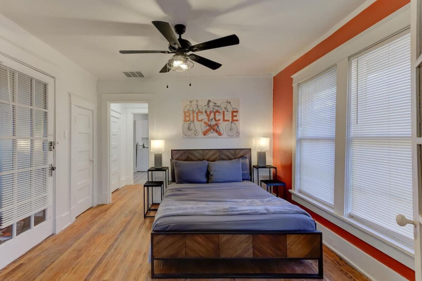 A bedroom with a bed, a ceiling fan, a bicycle-themed wall art, and a window with blinds.