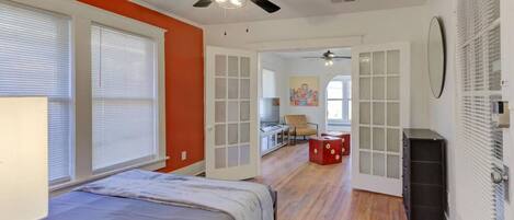 A bedroom with a bed, a ceiling fan, a window with blinds, and a door leading to another room.
