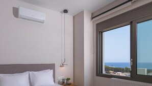A bedroom with a large bed, a window with a view of the sea, and a ceiling-mounted air conditioner. - Leon Luxury Home in Rethymno (Rethymno)