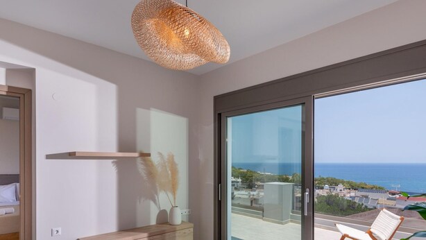 A modern living room with a large sliding glass door leading to a balcony with a view of the sea. - Leon Luxury Home in Rethymno (Rethymno)