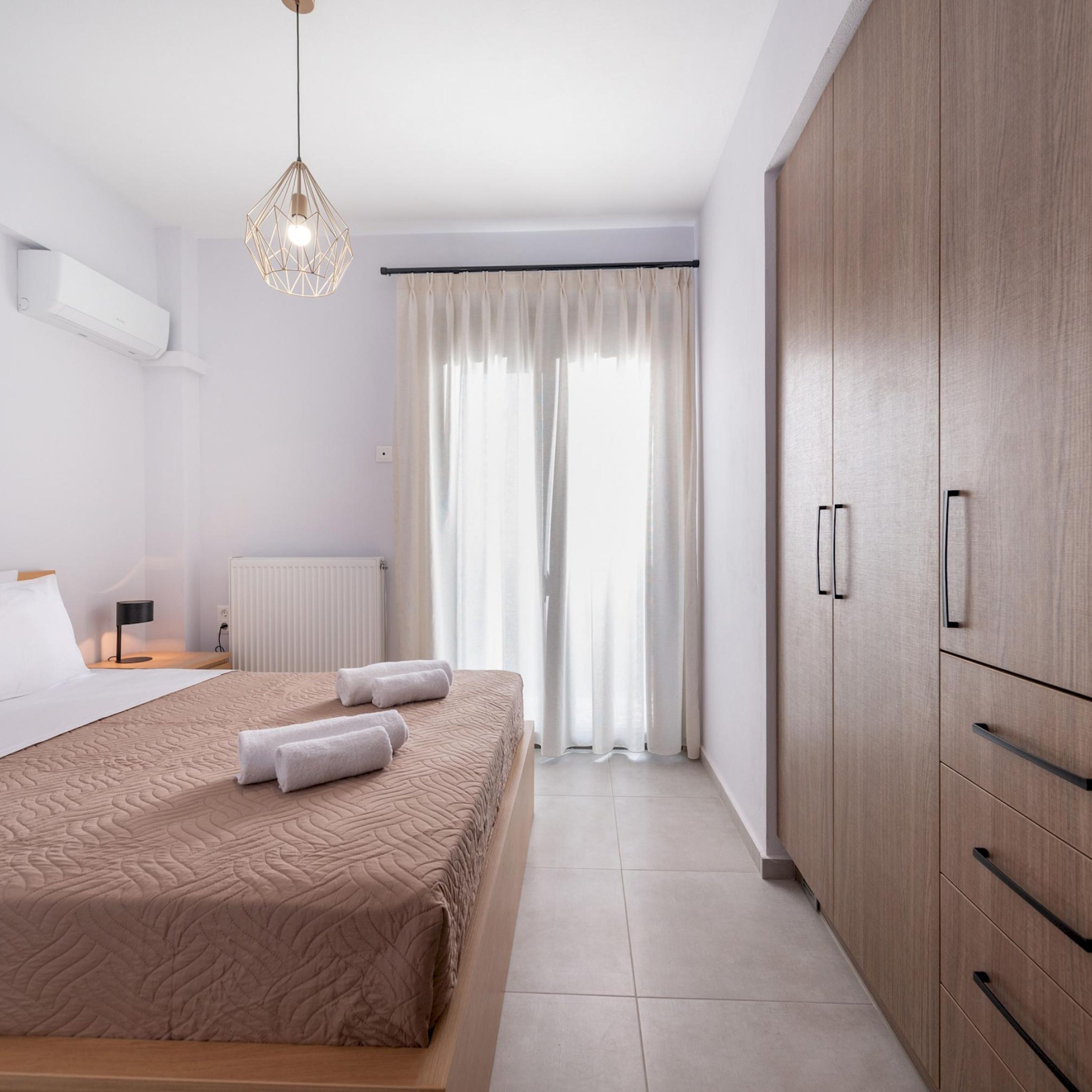 A modern bedroom with a large bed, a bedside table, a lamp, a radiator, and a wardrobe.