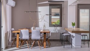 A modern dining area with a wooden table and chairs, a hanging light fixture, and a view of the outdoors through a window. - Leon Luxury Home in Rethymno (Rethymno)