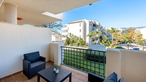 Ein Balkon mit einer Couch, einem kleinen Tisch und Blick auf eine Wohngegend mit Gebäuden und Bäumen.