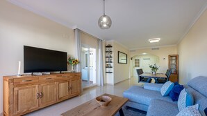 Ein Wohnzimmer mit Holzschrank, Fernseher, Sofa und Essbereich mit Tisch und Stühlen.
