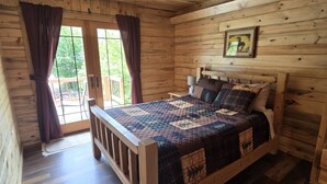 Une chambre à coucher dans une cabane en bois, avec un lit, des rideaux, un tableau accroché au mur et une vue par la fenêtre.