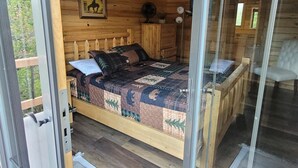 Une chambre dans une cabane en bois, avec un lit, une commode, un tableau encadré et une fenêtre.