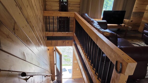 Un escalier en bois menant à un niveau inférieur, une rambarde en bois, une horloge et un téléviseur dans une pièce aménagée dans le style d’un chalet.