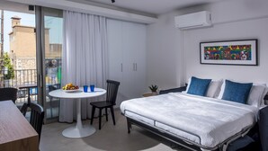A modern hotel room with a bed, a dining table with chairs, a small potted plant, and a window with curtains. - Athinais Apartments (Heraklion)