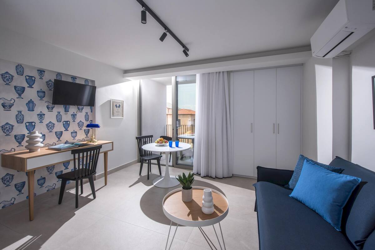 Ein modernes Wohnzimmer mit einer schwarzen Couch, einem runden Couchtisch und einem Essbereich mit weißem Tisch und Stühlen.