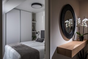 A modern bedroom with a bed, bedside table, and a mirror. - Athinais Apartments (Heraklion)