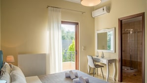 A hotel room with a bed, a desk, a chair, a shower, and a balcony with a view of greenery. - Villa Chrissi Kissamos (Kissamos)