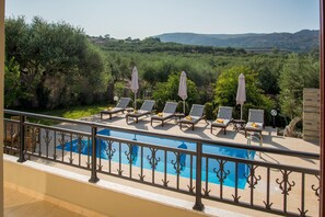 A poolside area with lounge chairs and umbrellas, overlooking a natural landscape with hills.