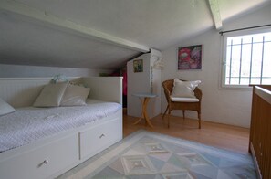 A bedroom with a bed, a chair, a small table, and a window.