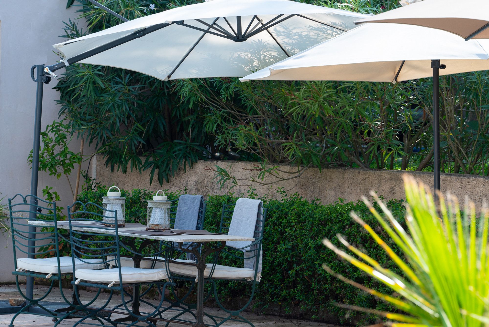 An outdoor patio with a table and chairs, a large umbrella, and lush greenery in the background.