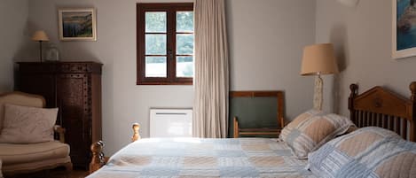 A bedroom with a large bed, a wooden chair, a dresser, a window with curtains, and a painting on the wall.
