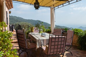 An outdoor patio with a table and chairs, a hanging lantern, and a view of a mountainous landscape.