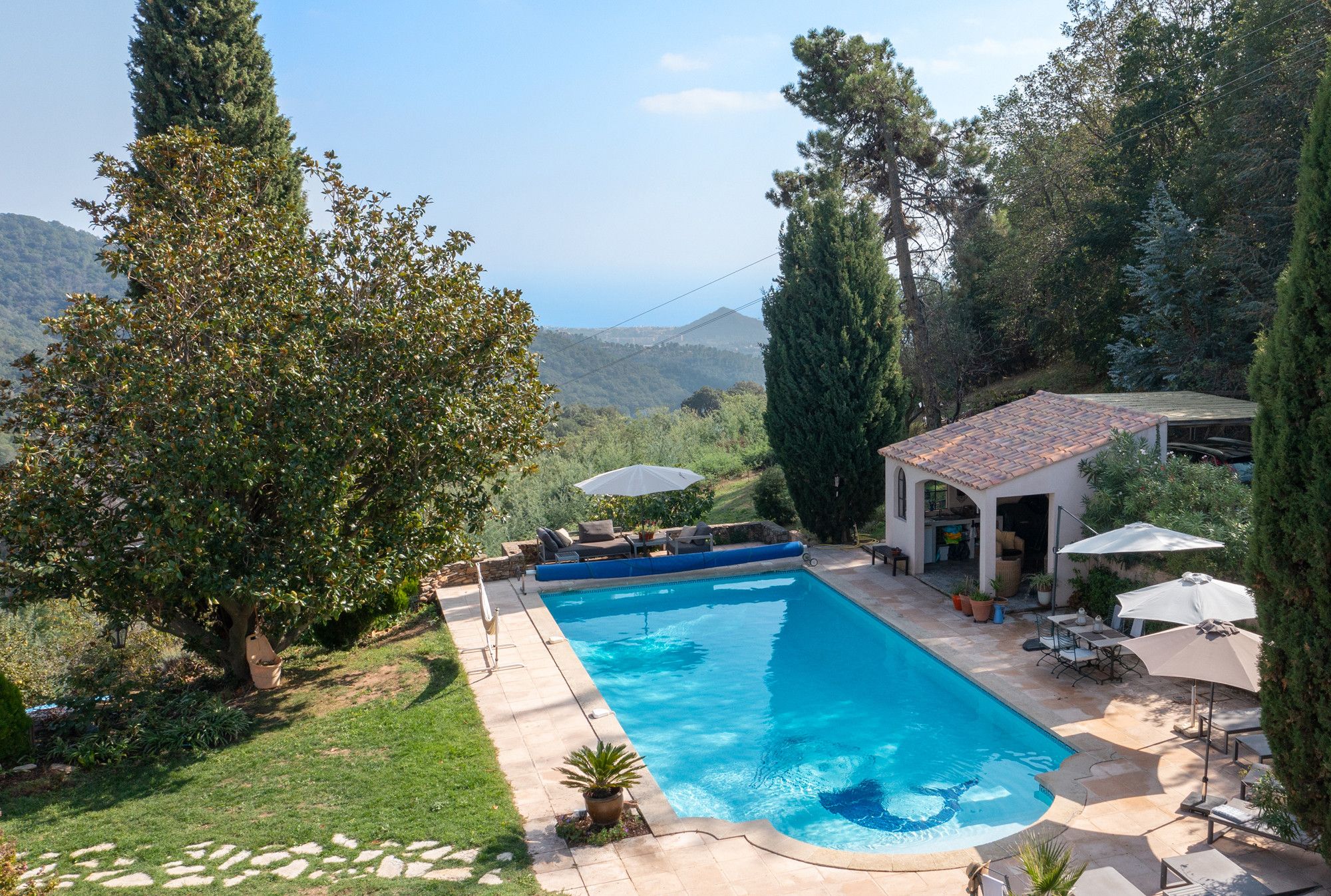 A rectangular swimming pool with a tiled deck, surrounded by a grassy area and trees.