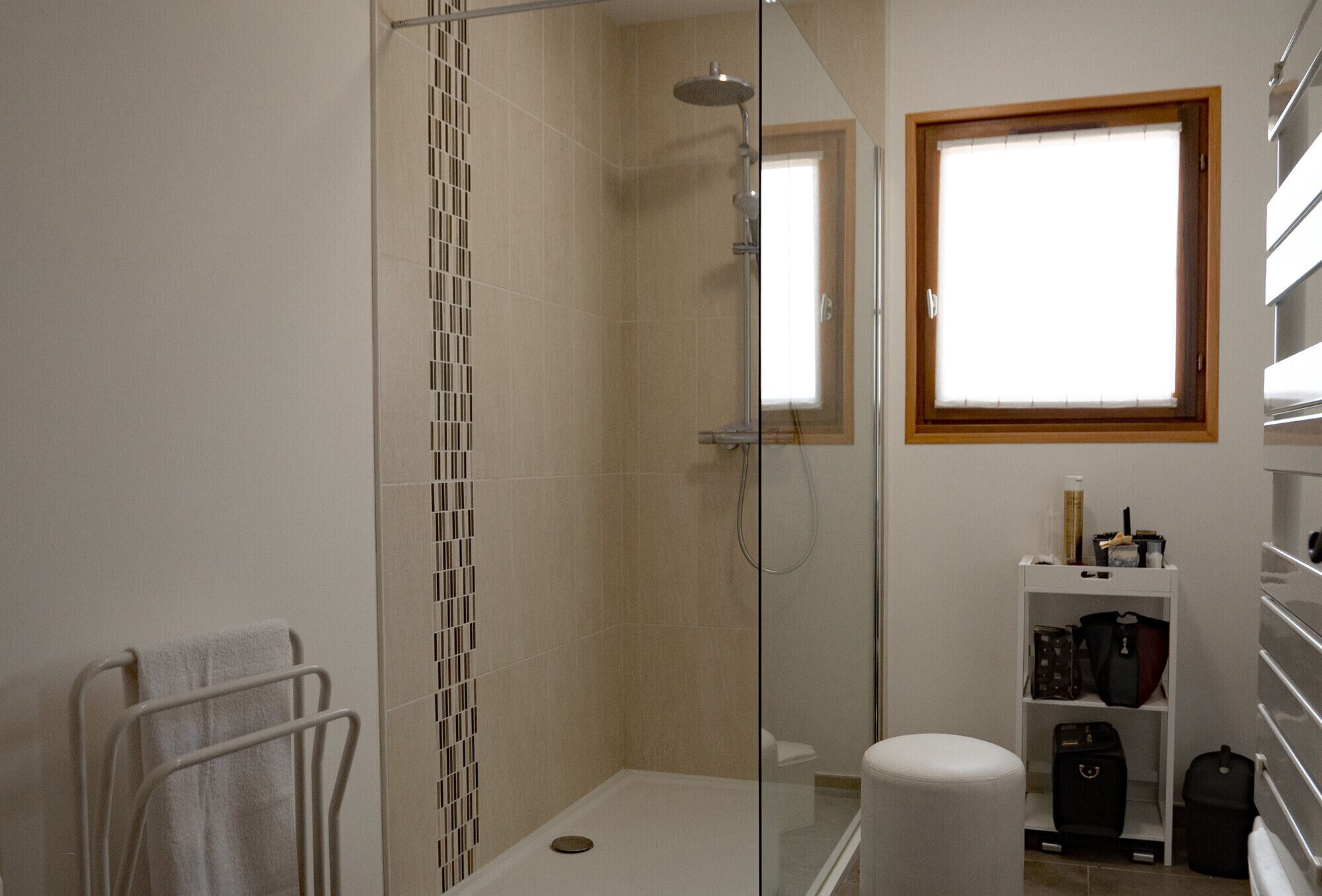 A modern bathroom with a glass-enclosed shower, a white toilet, and a shelf with luggage.
