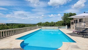 Une piscine rectangulaire à l’eau d’un bleu limpide, entourée d’une terrasse en pierre et d’une balustrade.
