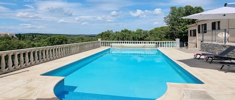 A rectangular swimming pool with a clear blue water surface, surrounded by a stone deck and a balustrade.