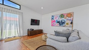 Ein Wohnzimmer mit grauem Sofa, einem Flachbildfernseher, einem farbenfrohen abstrakten Gemälde und einem Holzschrank.